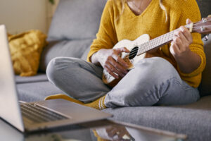 Close up of woman taking ukulele lessons online from her laptop during covid quarantine.